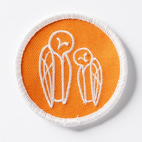 oranssi kangasmerkki jossa kaksi tyyliteltyä tornipöllöä.