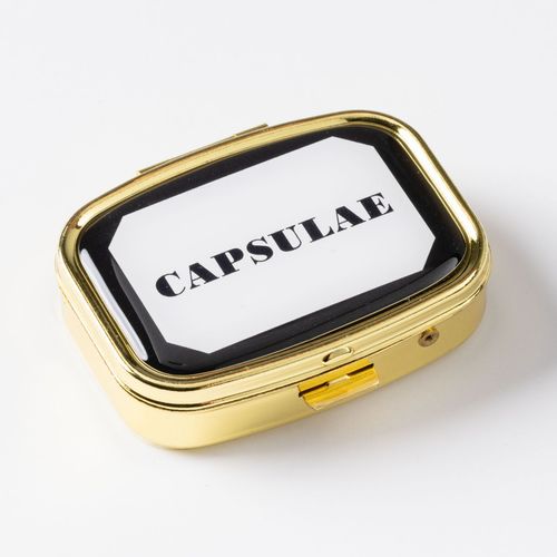 Guldfärgad pillerask med en etikettliknande text ”Capsulae”.